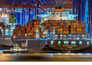 Cargo ship loaded with colorful containers docked at a port at night.