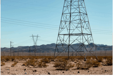 Power transmission towers in a desert landscape with mountains in the background.