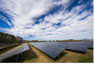 Rows of solar panels under a partly cloudy sky in a field.