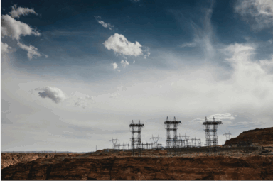 High-voltage transmission towers and power lines standing over a rocky desert landscape under a dramatic cloudy sky in Arizona.