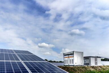 Solar panels and battery storage units under a partly cloudy sky.